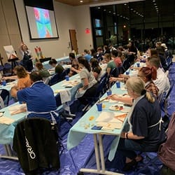 A room full of people painting an autumn scene at Homecoming's Paint Night.