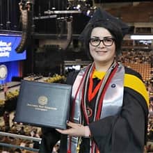 Janet Johnson dressed in cap and gown and holding a diploma at her SNHU Commencement ceremony