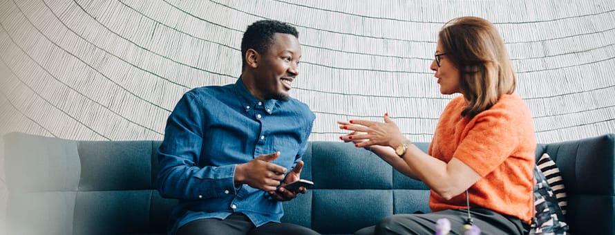 Two colleagues sitting on an office couch, discussing how to improve communication skills at work.