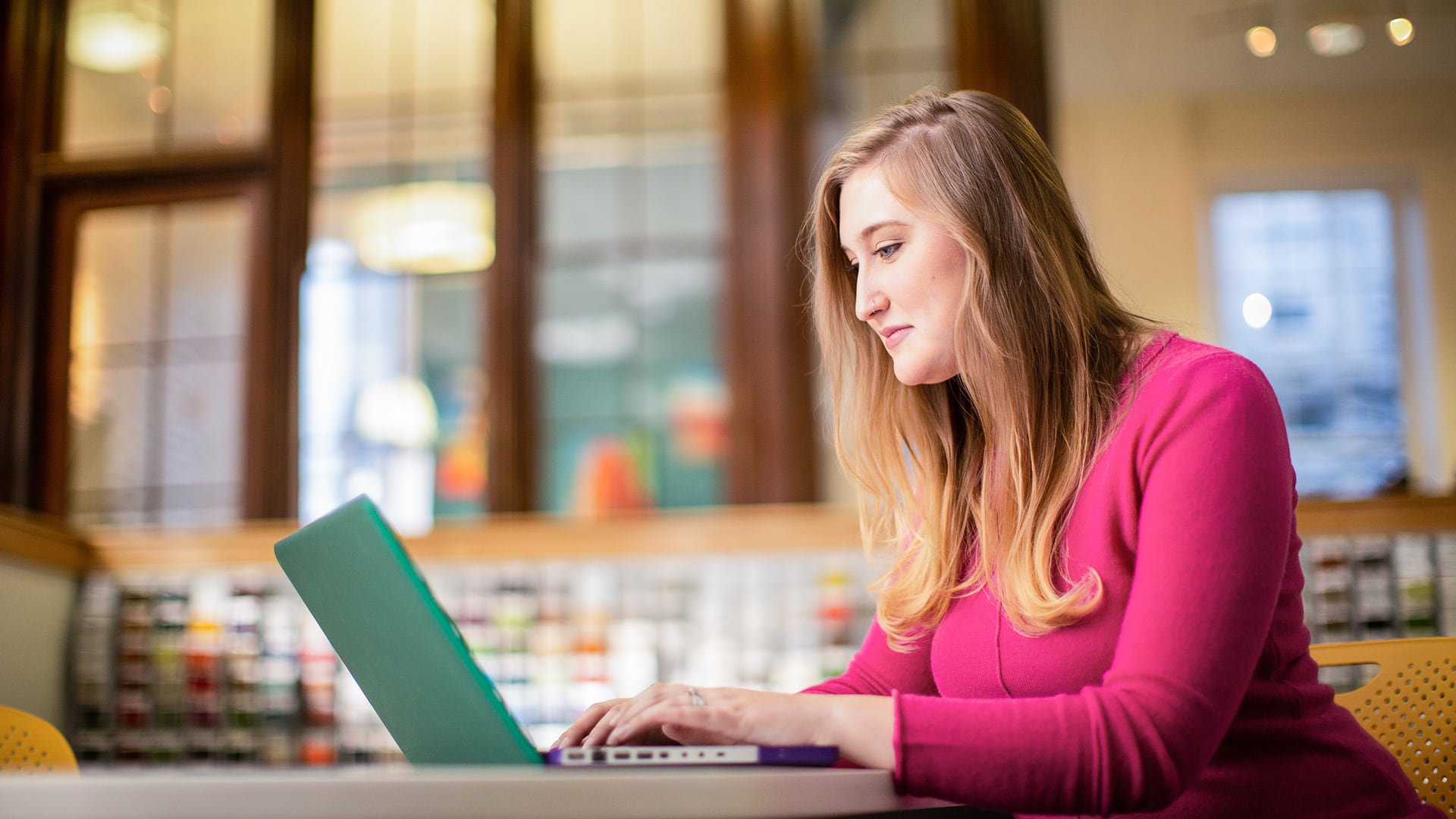 Caitlyn Carey, who earned her degree from SNHU in 2015, wearing a pink sweater and typing on her laptop. 