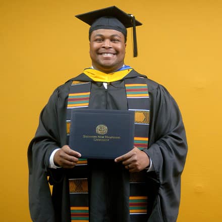 Aaron Davenport, a 2025 master's in finance graduate from SNHU, wearing a cap and gown and holding his diploma.