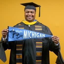 Aaron Davenport, a 2025 master's in finance graduate from SNHU, wearing a cap and gown and holding a Michigan state flag. 