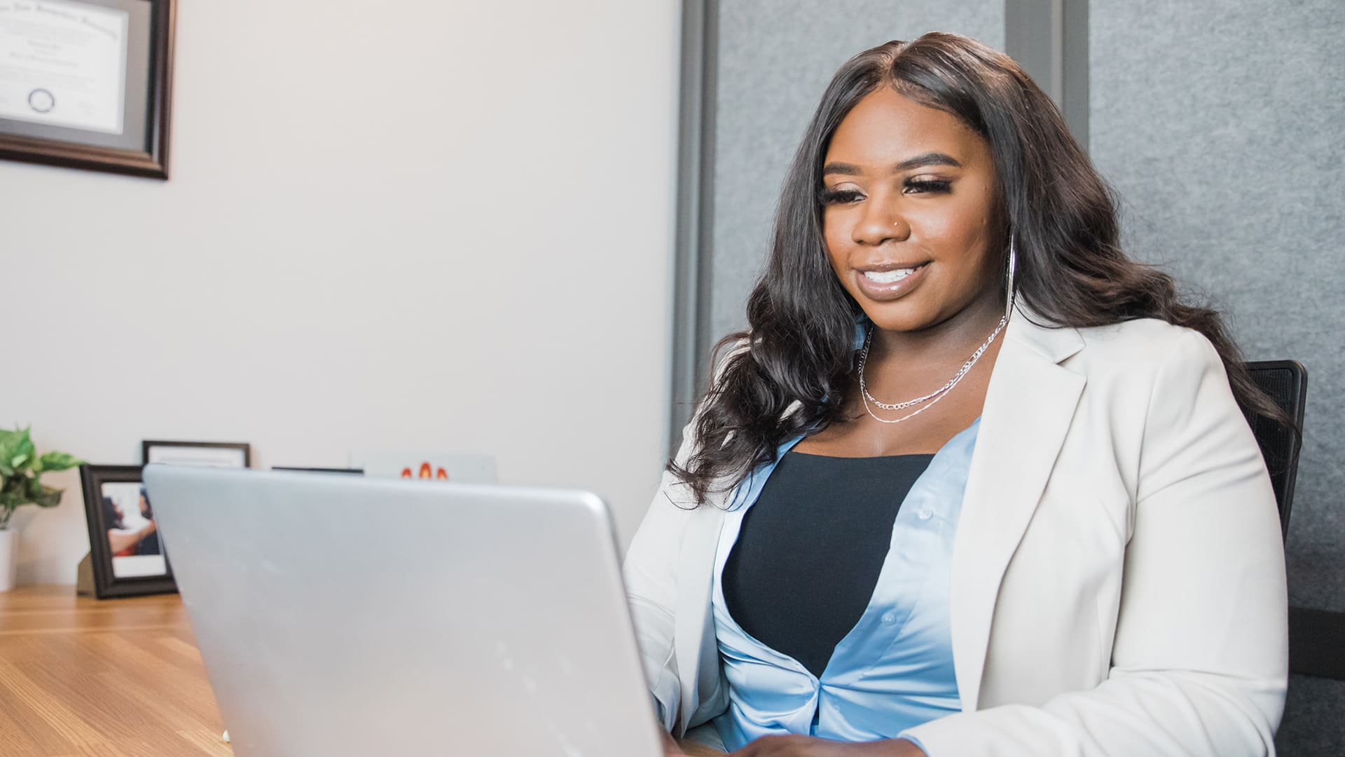 Tanzania Fair, wearing a white blazer, sitting at a table and typing on a laptop.