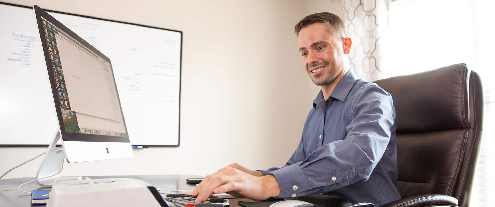 Blake Venable, who earned his accounting degree from SNHU, sitting at an office desk with a large computer monitor and typing on a calculator.