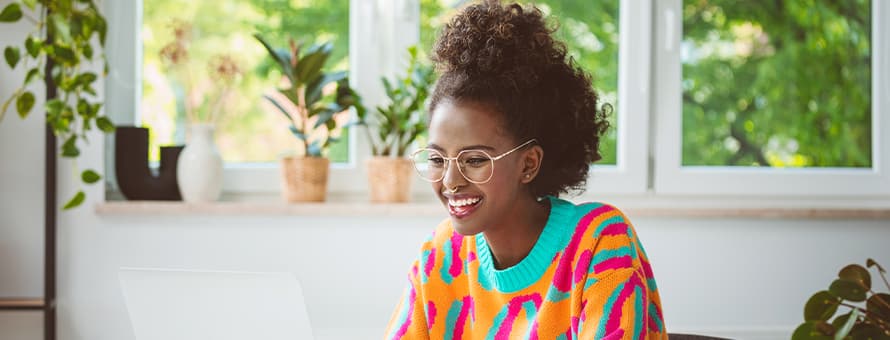 An undergraduate student wearing a bright orange shirt, completing her accelerated master's program coursework on a laptop