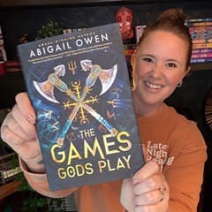 Ali Lamoureux, an SNHU bachelor's in healthcare administration graduate, holding "The Games Gods Play" by Abigail Owen.