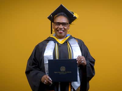 Angela Charlton, who earned her bachelor's in computer information systems from SNHU in 2025, wearing her cap and gown and holding her diploma in front of a yellow backdrop.