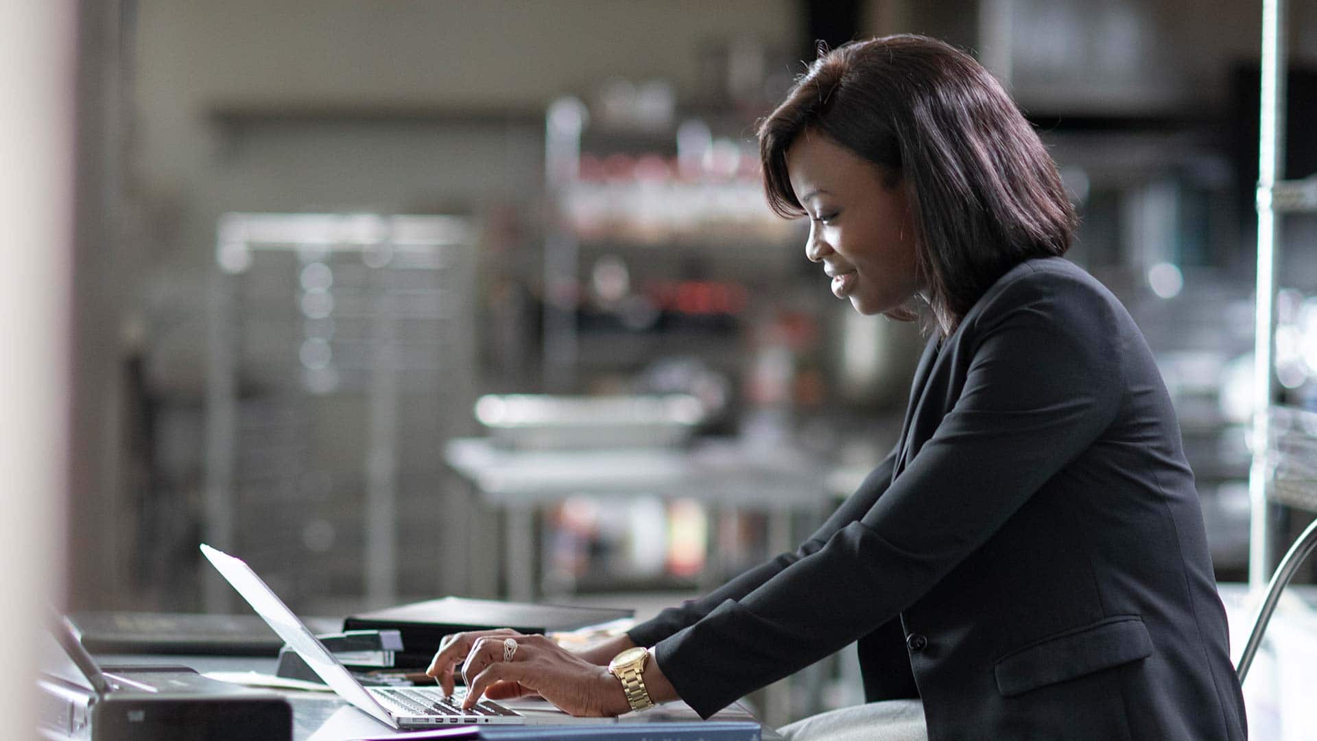 Sierra Ingram, who earned her degree from SNHU in 2018, wearing a dark blazer and gold watch, typing on a  laptop computer. 