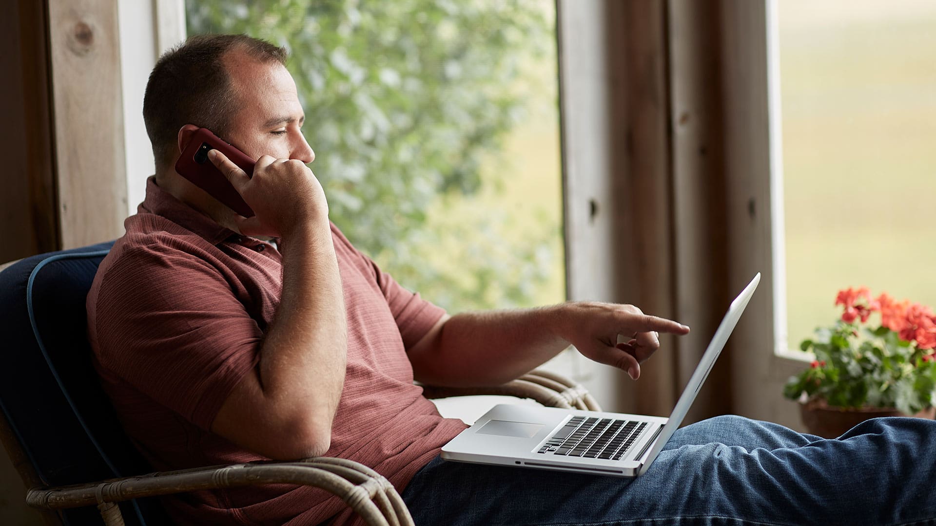 Raymond Gammon, who earned a dgree from SNHU in 2020, holding a cell phone to his right ear and pointing to his laptop screen on his lap.