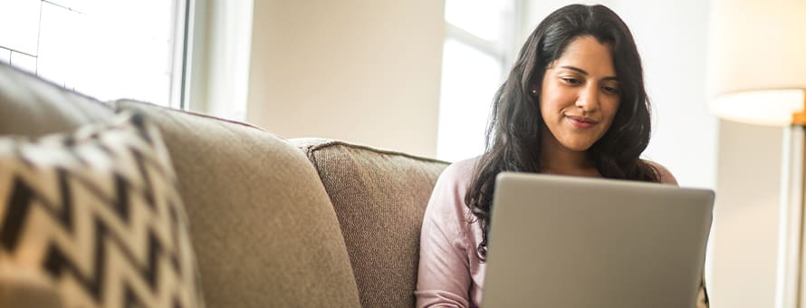 A woman sitting on a couch with her laptop working on her associate of arts degree