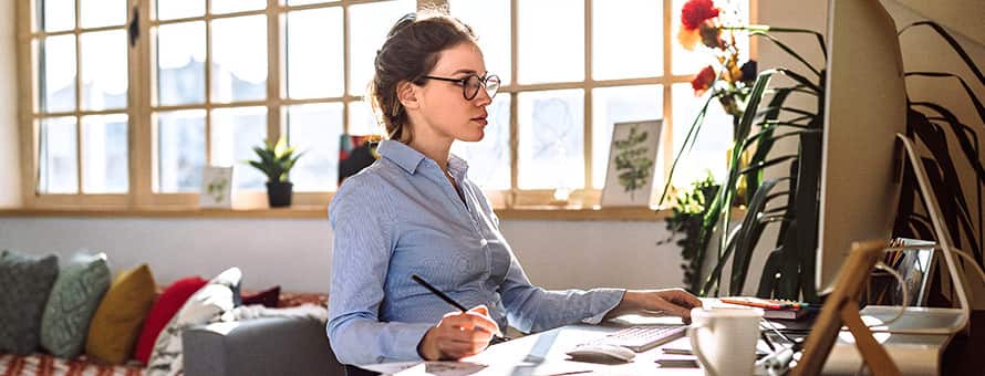 An online instructor sitting at a desk and looking at a computer as she video conferences with an online student.
