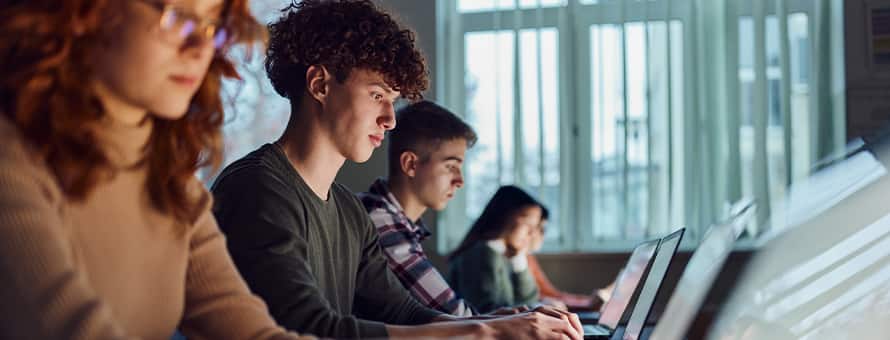 A group of students sitting in a row working on laptops