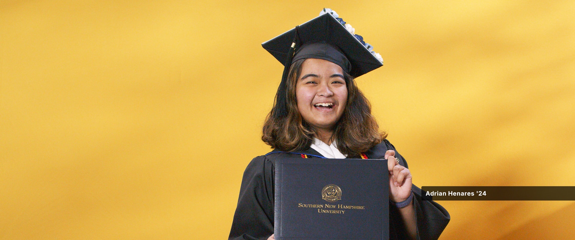 Adrian Henares, who earned her bachelor's in communications from SNHU in 2024, wearing her cap and gown and holding her diploma.