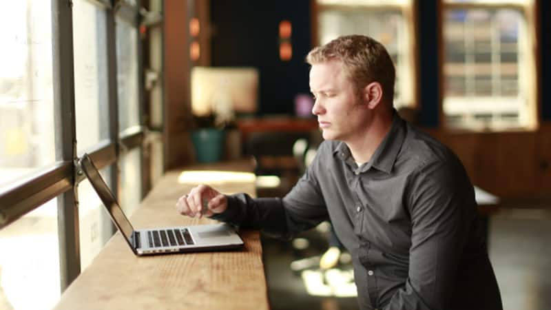 Shawn Espeland, who earned his degree from SNHU, sitting at a wooden table typing on a laptop computer.