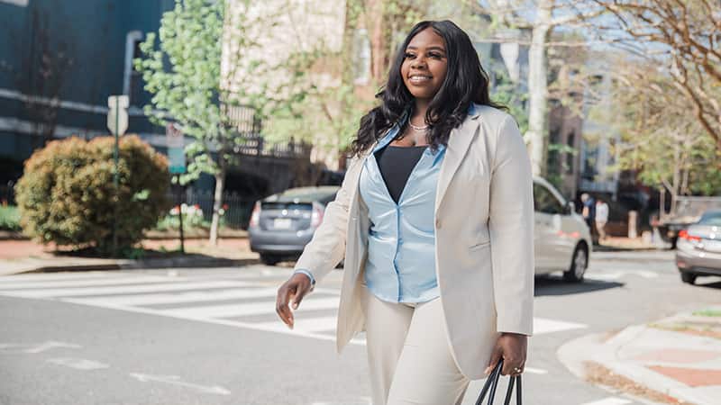 Tanzania Fair, who earned her degree from SNHU in 2020, crossing a city street and carrying a handbag.
