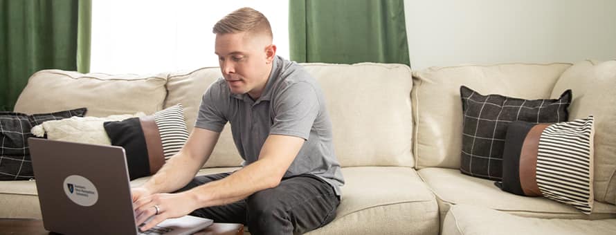 Rob Thomas, a 2024 graduate from SNHU, sitting on a couch and typing on a laptop.