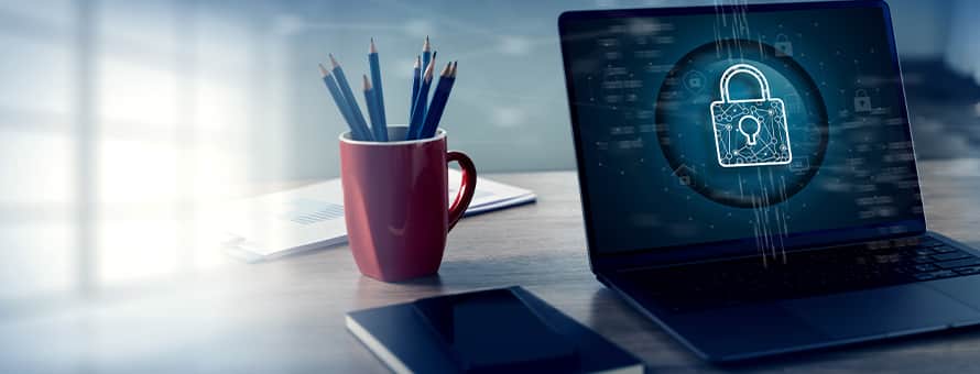 A laptop with a lock on its screen sitting on a desk by a notebook and cup of pencils.