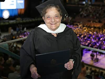Mary Beth Dayley, who earned her online master's in creative writing from SNHU in 2024, wearing her cap and gown and holding her diploma.