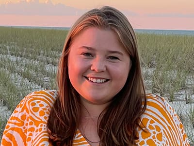 Bridget Gallagher, who earned her online associate in marketing in 2021, wearing a white and orange blouse, standing in an open field.