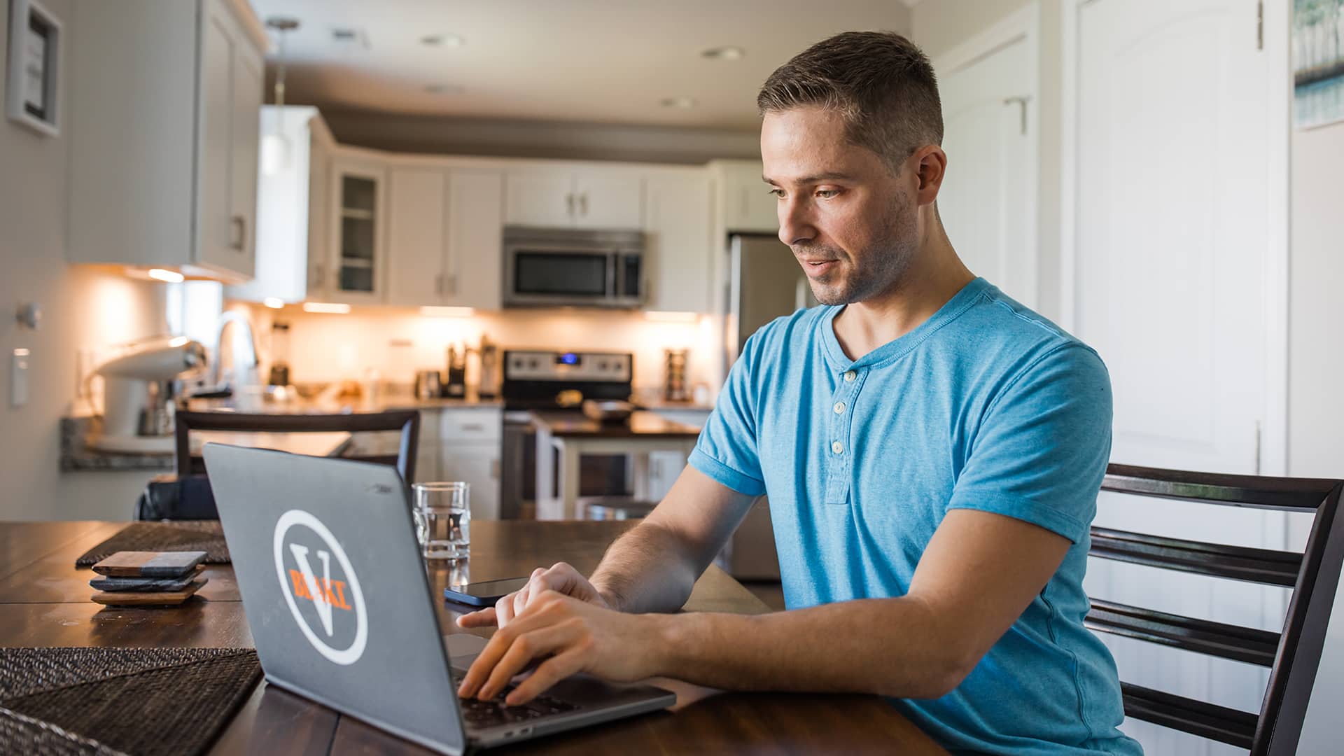 Blake Venable at his kitchen table working on his laptop with a glass of water beside him.