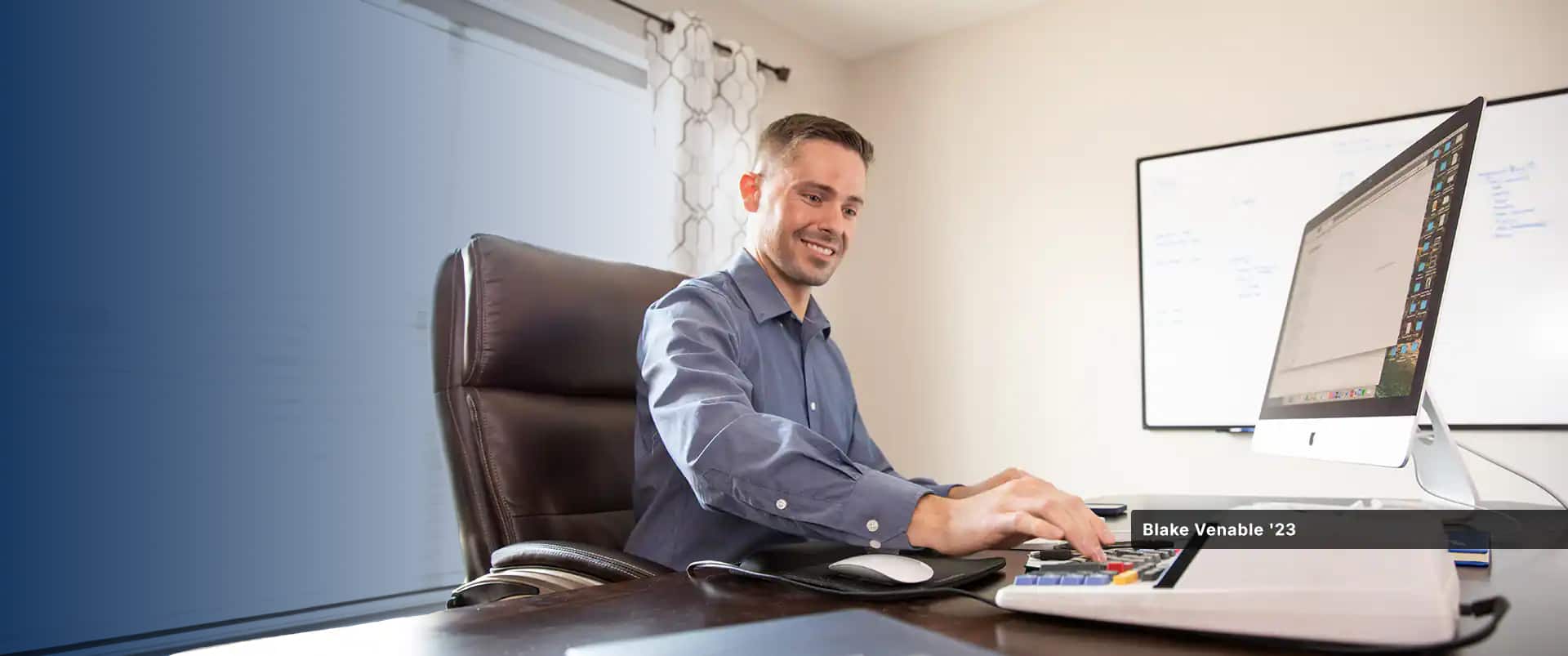 Blake Venable, who earned his accounting degree from SNHU, sitting at an office desk with a large computer monitor and typing on a calculator.