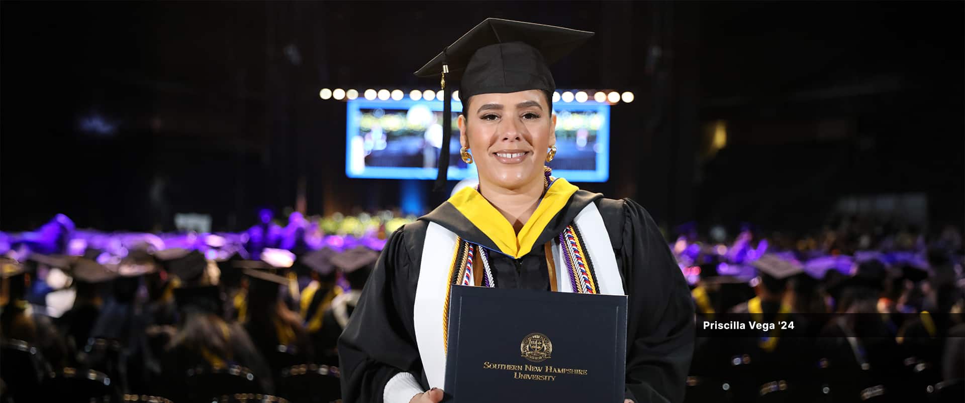 Priscilla Vega, who earned her bachelor's in business administration with a concentration in organizational leadership from SNHU in 2024, wearing her cap and gown and holding her diploma.