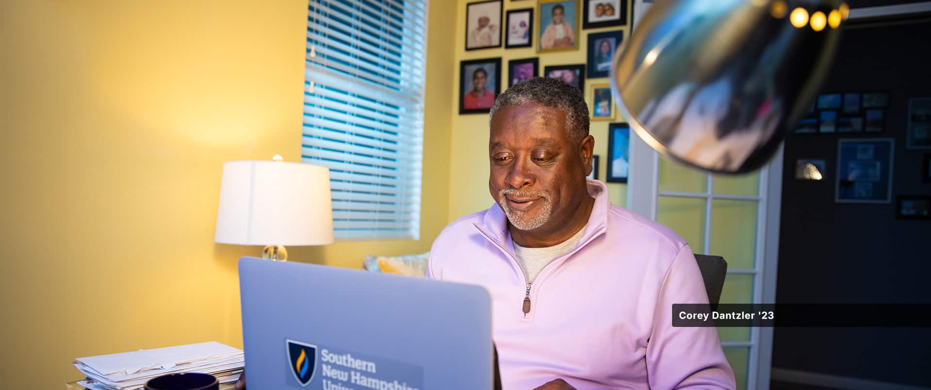 An SNHU student sitting in a home office, typing on a laptop with the Southern New Hampshire University logo on it