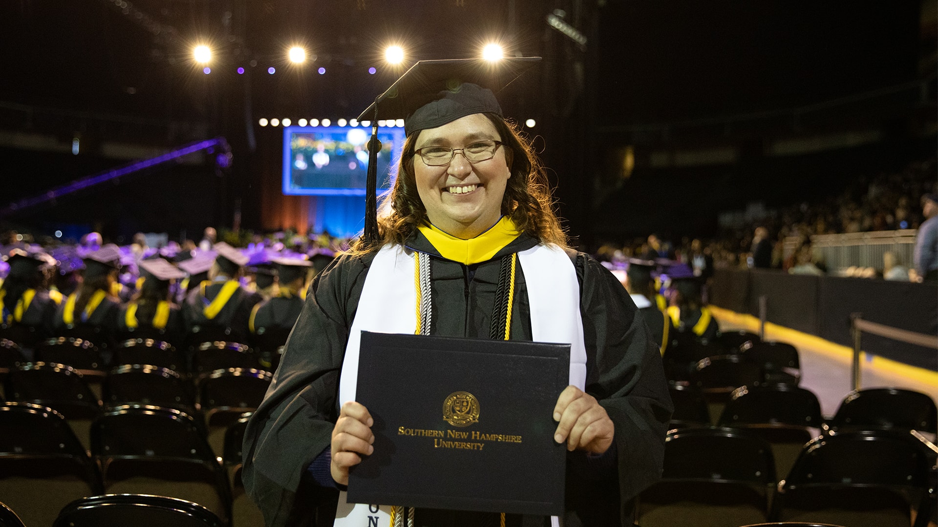 Karie Lamb, who earned her degree from SNHU in 2023, wearing her cap and gown and holding her diploma at the SNHU commencement