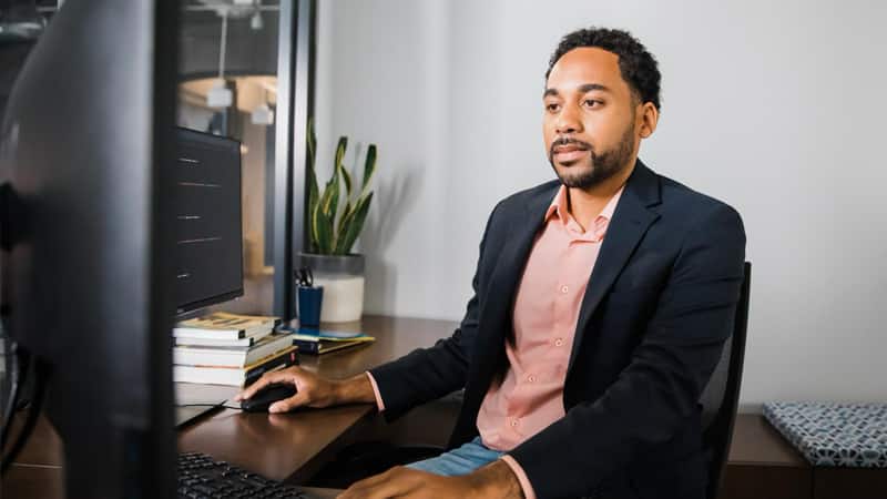 2022 online degree graduate Gary Walker, standing in front of a laptop with a pair of headphones resting on his shoulders.