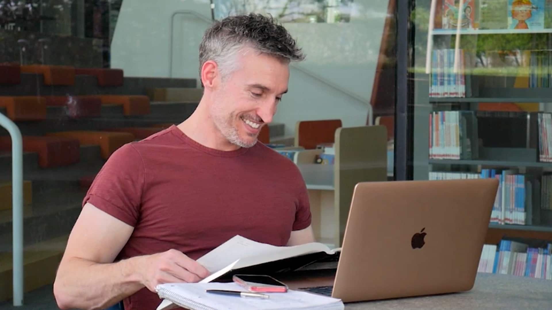 BS in Computer Science degree with a software engineering graduate Jef Dewitt, looking through a book while sitting at a computer desk.