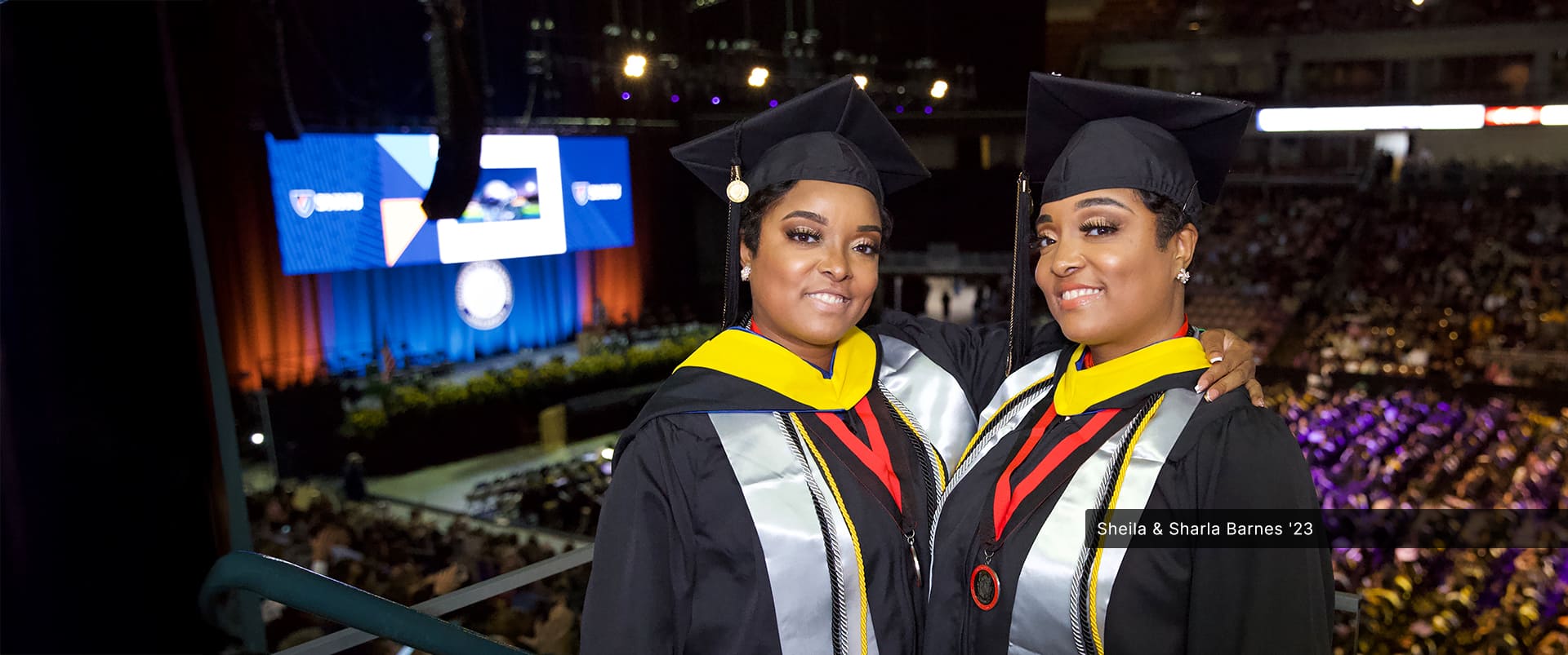 Sheila and Sharla Barnes, identical twins who both earned their bachelor's in criminal justice from SNHU in 2023, wearing their cap and gowns at the SNHU commencement ceremony.
