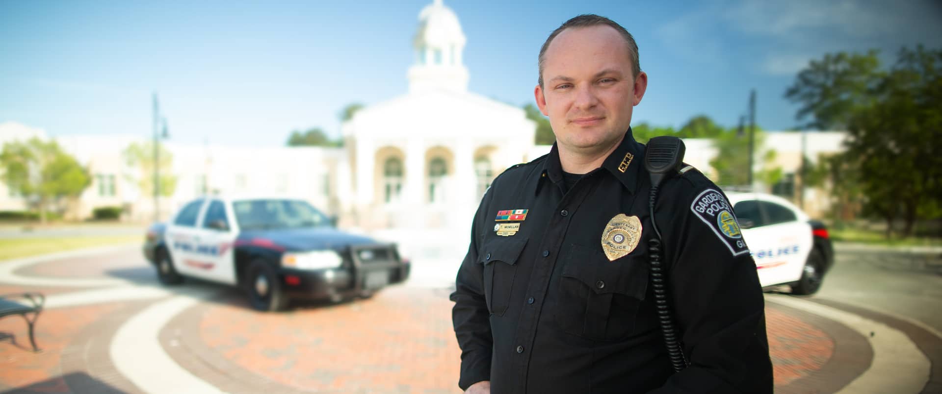 Tim McMillan, who earned his degree from SNHU in 2015, wearing his police uniform with a police cruiser in the background.