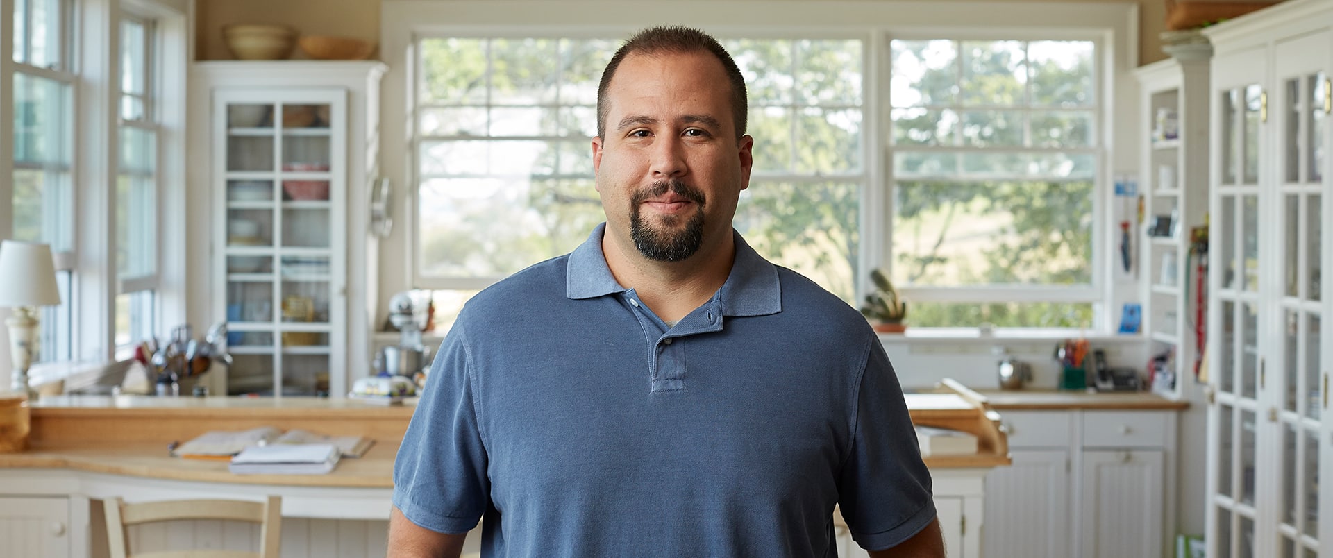 Raymond Gammon, who earned a data analytics degree in 2020, standing in his kitchen wearing a blue polo shirts.