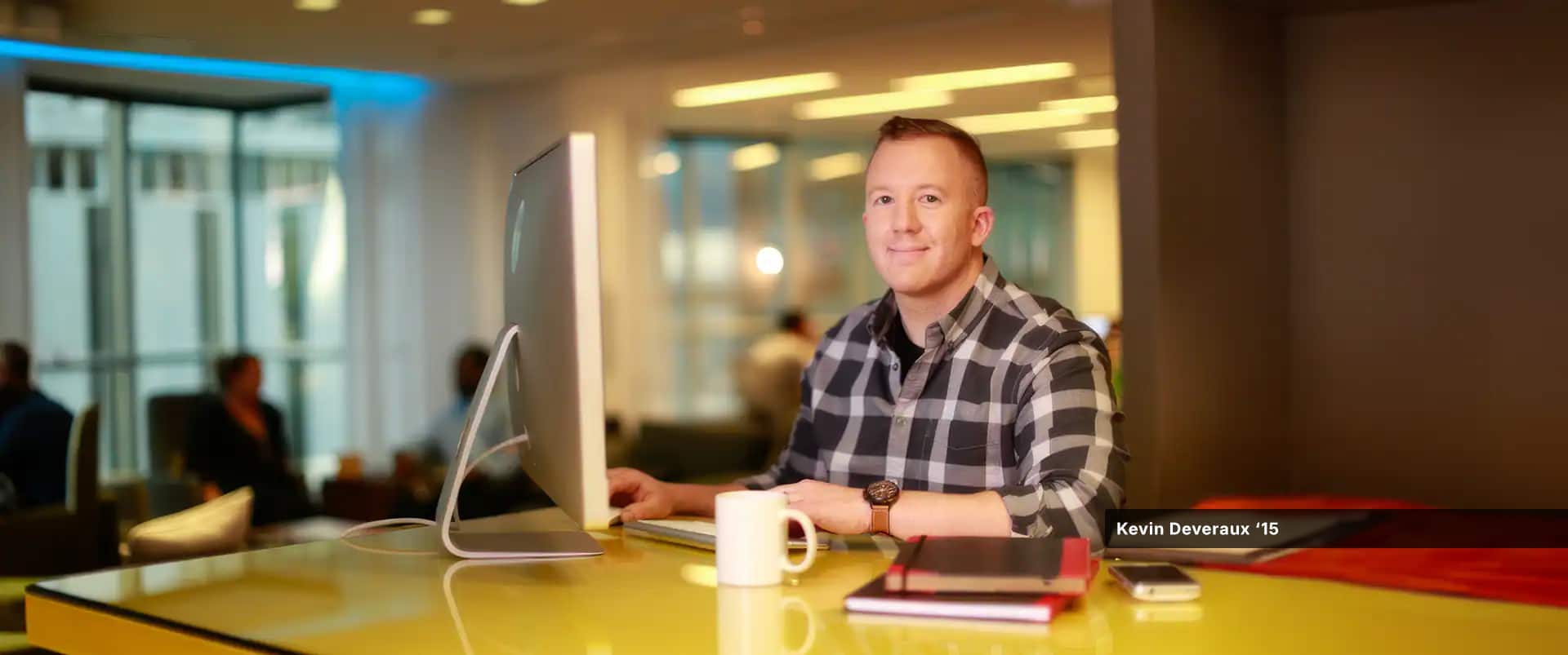 Kevin Deveraux, who earned his finance degree from SNHU, at his computer with two thin notebooks, a smartphone and cup of coffee on the table in front of him.