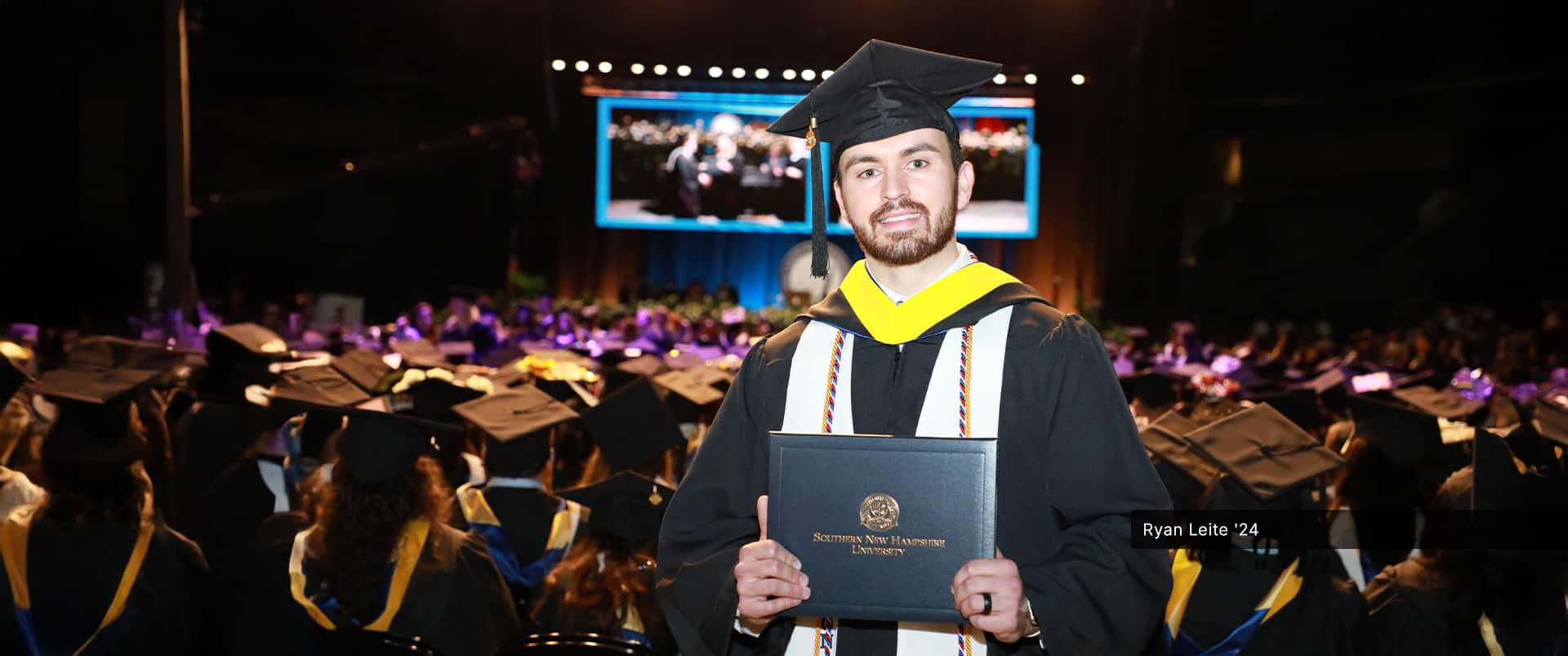 Ryan Leite, who earned his bachelor's in health sciences from SNHU in 2024, wearing his cap and gown and holding his diploma at the SNHU commencement ceremony.