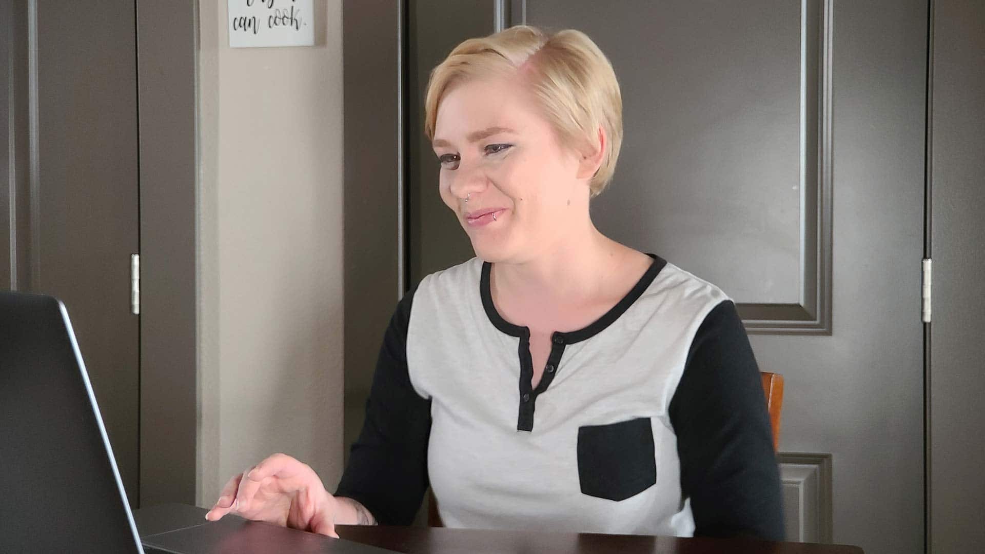 Jolene Stetz, who earned her degree from SNHU in 2021, wearing a grey and black long-sleeve T-shirt in her kitchen working on her laptop.