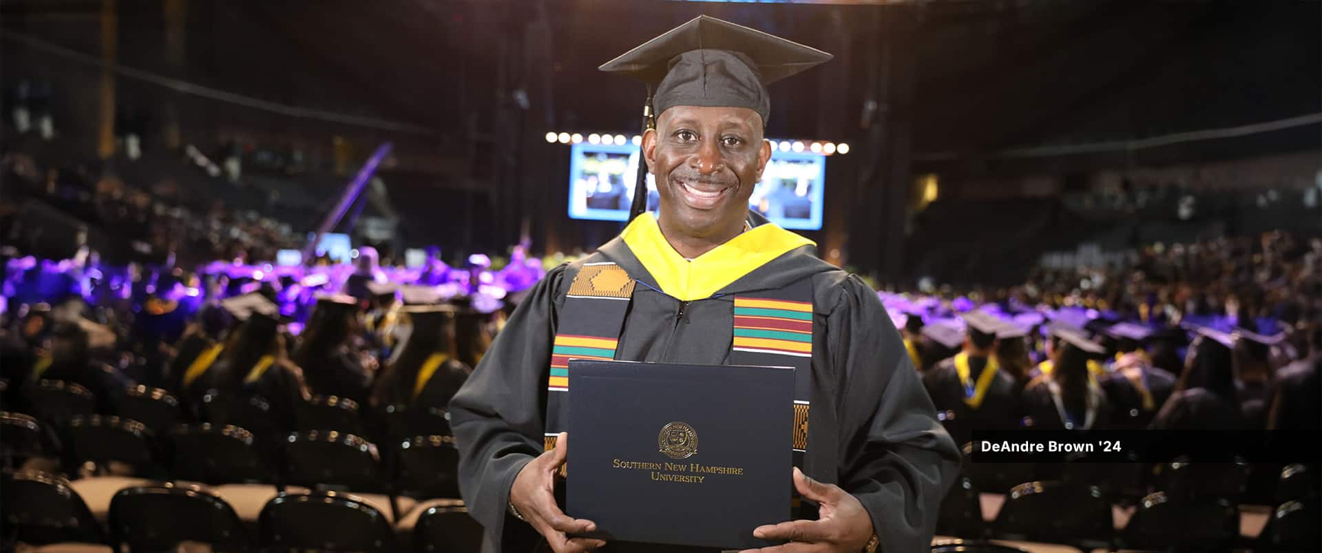 DeAndre Brown, who earned his bachelor's in operations management from SNHU in 2024, wearing his cap and gown and holding his diploma at SNHU's commencement ceremony.