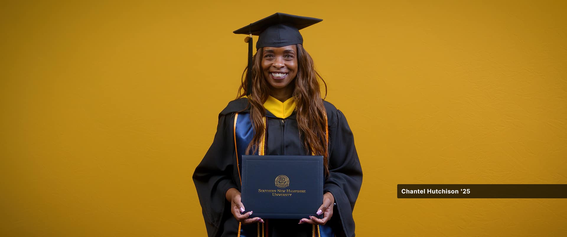 Chantel Hutchinson, who earned her bachelor's in public health from SNHU in 2025, wearing her cap and gown and holding her diploma in front of a yellow backdrop.