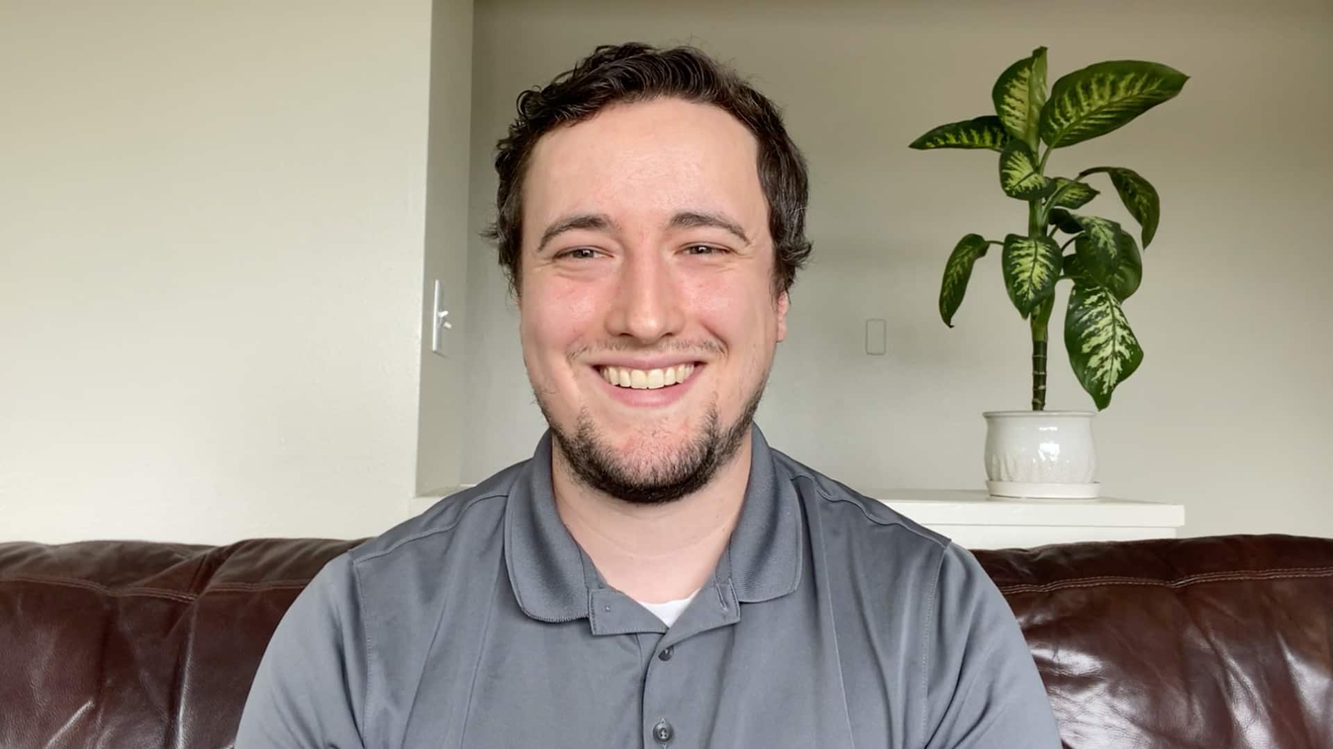 Nick Gardner, who earned his degree from SNHU in 2019, sitting on a brown leather couch with a house plant on a table behind him.