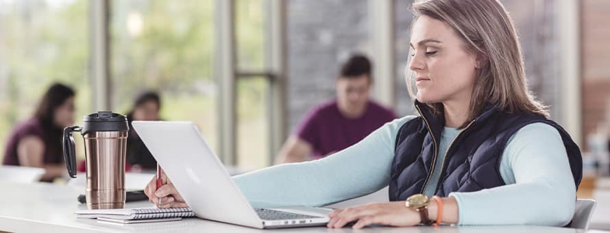 A student who is earning a BS degree, taking notes as she studies on a laptop in the SNHU library