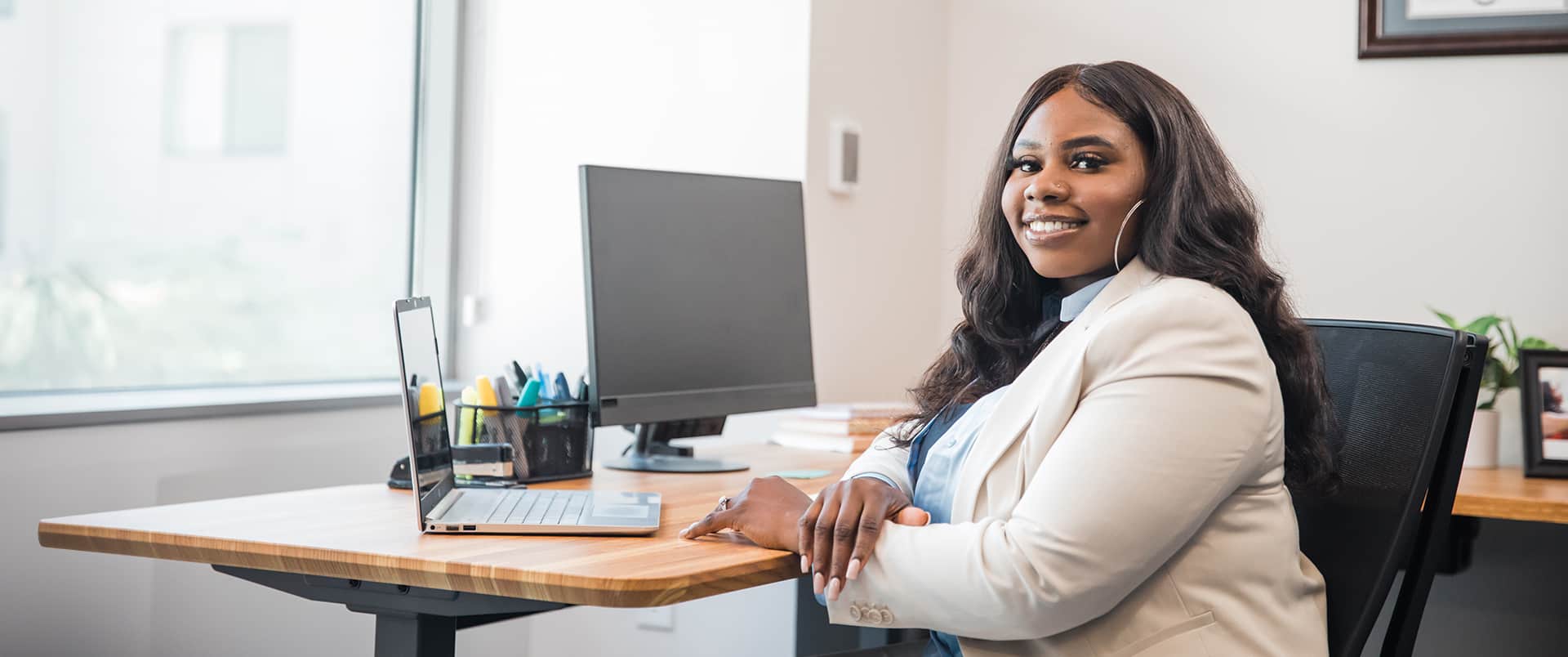 Tanzania Fair, who earned her degree at SNHU, sitting at an office desk with a computer monitor, a laptop and pen case in the background.