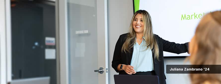 Juliana Zambrano '24, dressed professionally in a blouse and blazer, presenting in front of a screen in a boardroom.