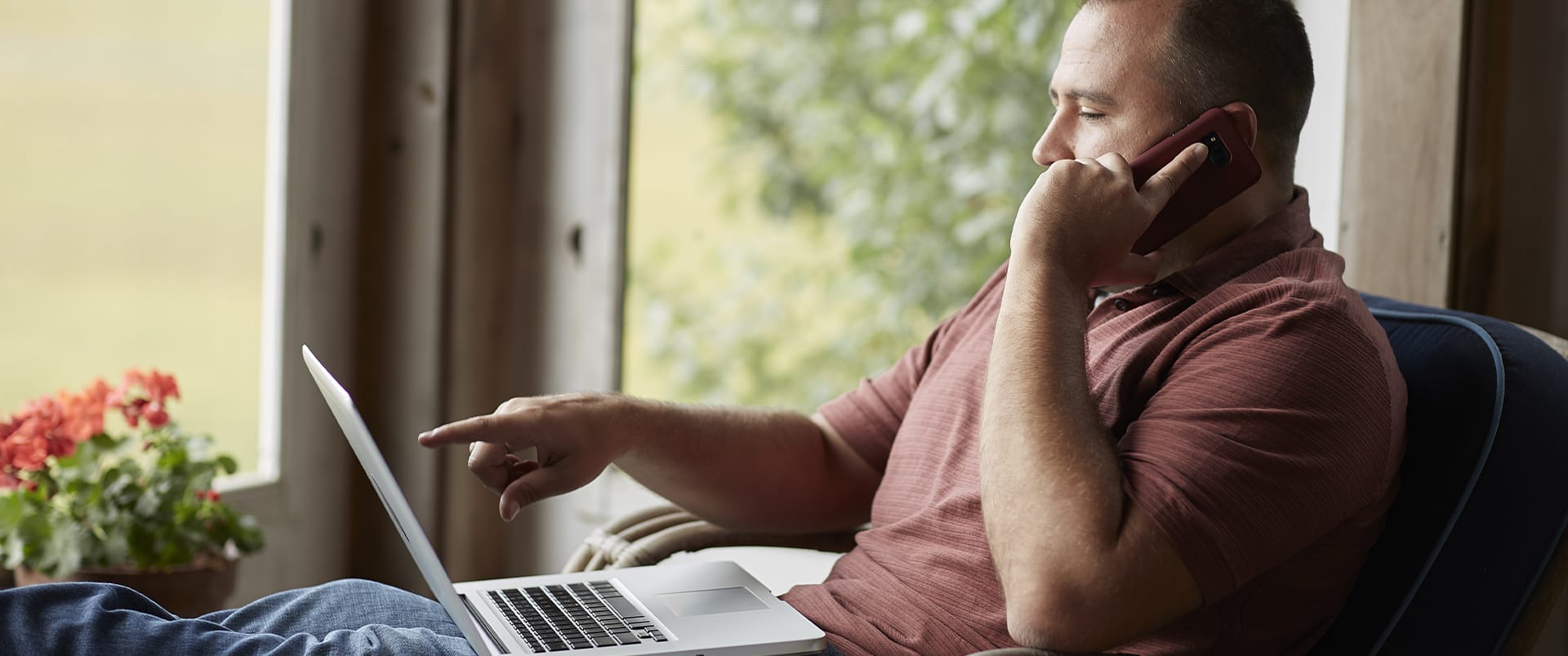 Raymond Gammon, who earned his degree from SNHU in 2020, sitting on a screened porch holding a cell phone to his left ear and pointing at his laptop screen.