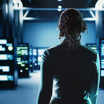 A woman walking into a dark computer lab glowing in blue.
