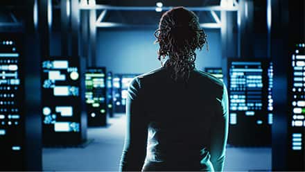 A woman walking into a dark computer lab glowing in blue.