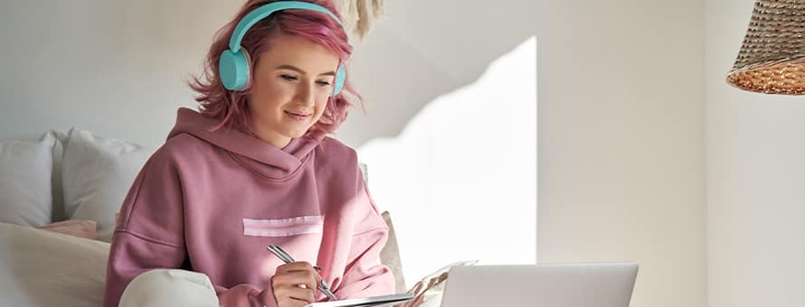 A person wearing a pink sweatshirt and teal headphones, researching on a laptop which graduate program to choose.