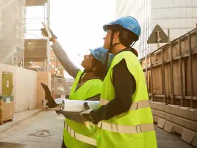 Two workers wearing hard hats and high visibility vests looking at a construction site.