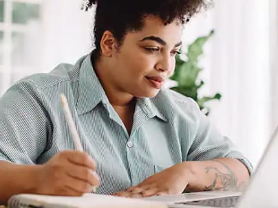 An SNHU student holding a pen while looking at a laptop at home.