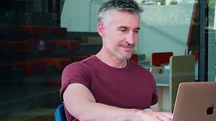 Jef Dewitt '22, who graduated from an online computer science program at SNHU, working at a laptop in a library.