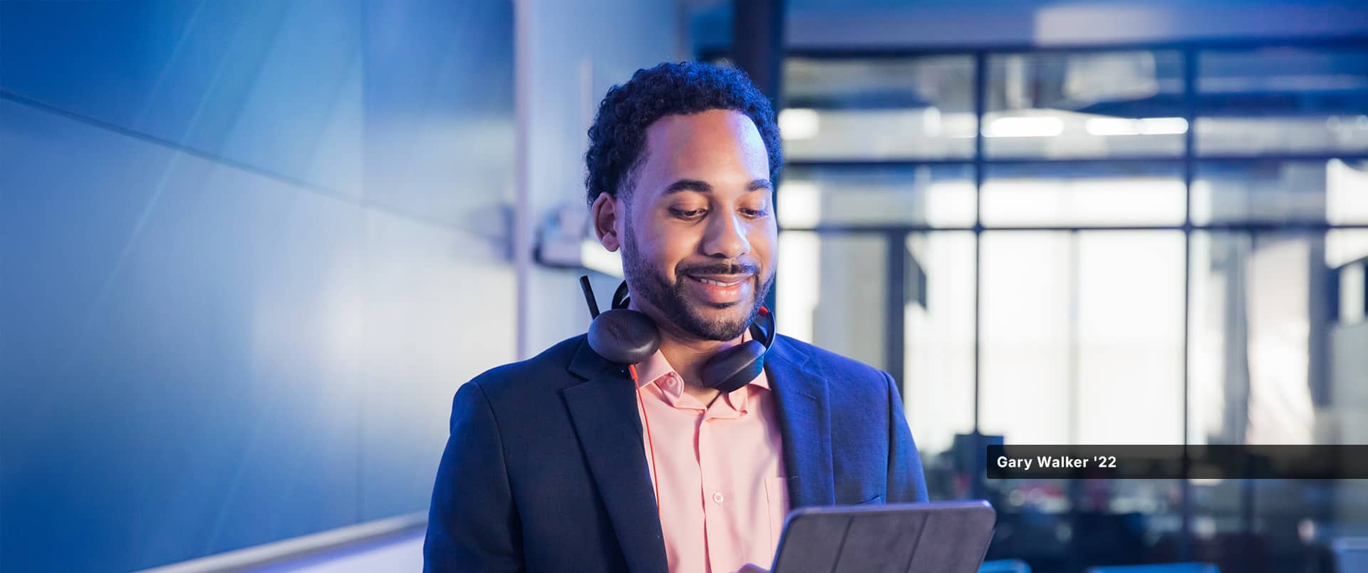 Gary Walker, who earned his degree from SNHU in 2022, looking at a tablet computer and wearing a pink button-down shirt, blue sports coat and a headset around his neck.